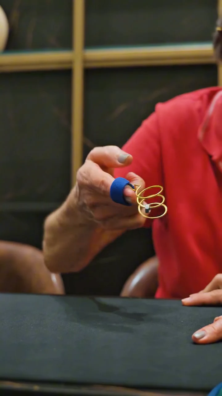 Mão de uma paciente fazendo exercício para os dedos com uma mola, sobre uma mesa escura